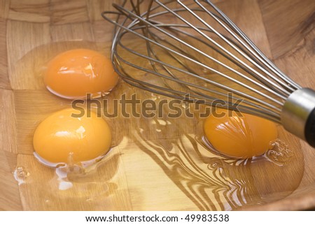 Three eggs and a whisk in a bowl ready to be whisked.