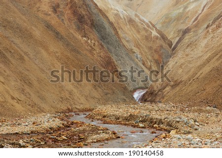Marsian landscape with lifeless orange and yellow hills and river running among them during the sand storm, Iceland