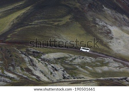 View of the white 4x4 bus from above on a road in highlands among green moss, Iceland