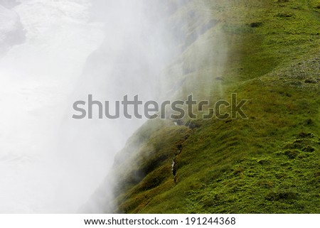 White thick steam and bright green hill covered with fresh moss, Gulfoss waterfall, Iceland