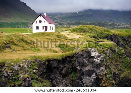 Beautiful white house standing among the clffs covered with grass and moss, West Iceland