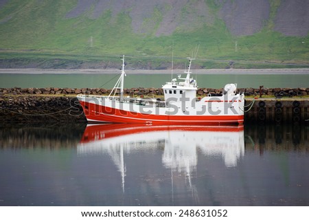 Small red and white fishing boat reflecting in the still sea, Arnarstapi, West Iceland