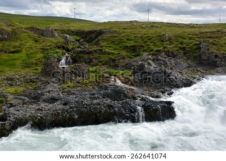 Rocky river show covered with moss and grass near Godafoss waterfall on a cloudy day, North Iceland