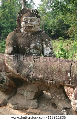 A stone guardian holds a large snake to keep evil spirits away from the temples of Angkor Wat in the Cambodian jungle.