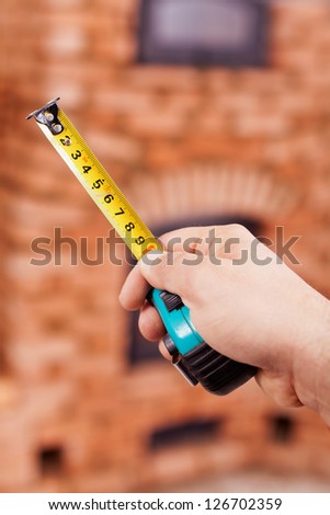 Masonry worker hand holding tape measure - closeup with brick structure in background
