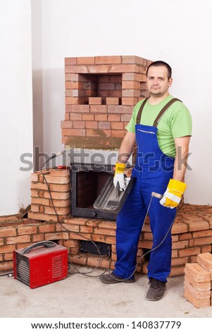 Worker mounting the door of a brick masonry heater with a welding equipment