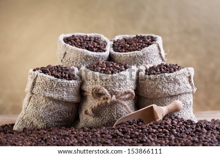 Roasted coffee beans in small burlap bags - on golden background