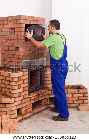 Worker in uniform building a traditional stove from bricks - fitting the doors