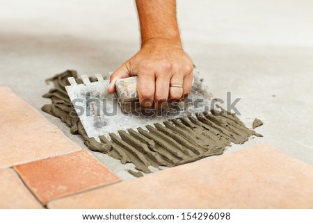 Laying ceramic floor tiles - man hand spreading adhesive material, closeup