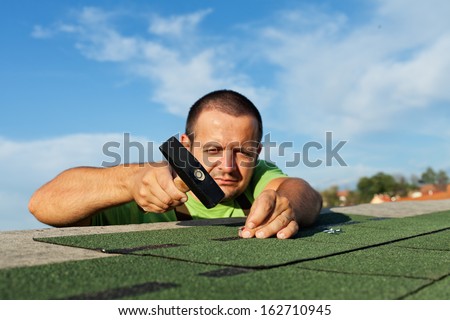 Man installing bitumen roof shingles - using a hammer and nails