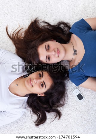 Two young women sharing a music player - laying on the floor with heads touching