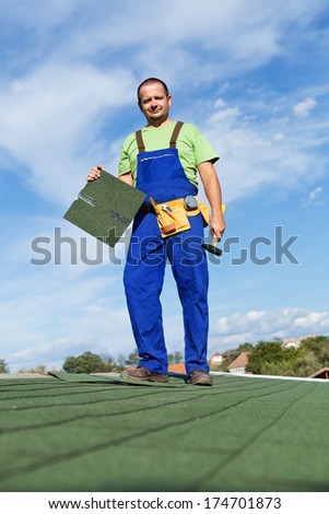 Worker installing bitumen roof shingles - standing on top of building