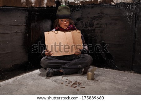 Begging homeless child sitting with a blank sign and some change in a dark corner