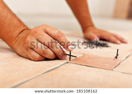Worker hands placing spacers between ceramic floor tiles - close up
