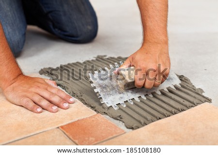 Worker hands spreading adhesive for ceramic floor tiles - closeup
