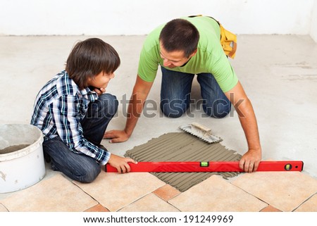 Man laying ceramic floor tiles on concrete - checking his work with a spirit level