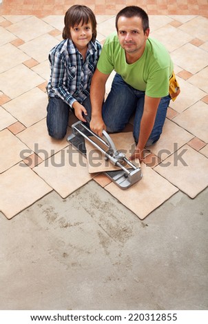Father and son laying ceramic floor tiles together - working with a cutter