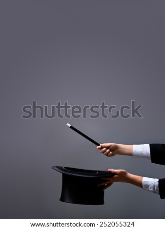 Magician hands holding hat and magic wand on gray background - with lots of copy space