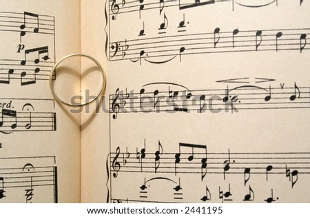 Golden wedding ring on old sheet music, casting a heart shaped shadow