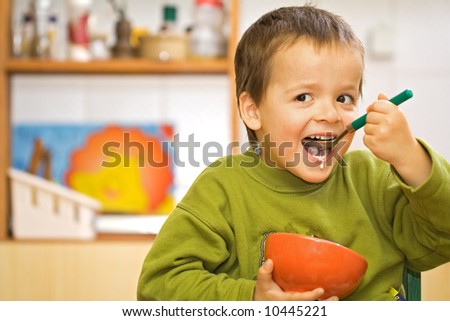 Happy boy eating cereals with milk in the kitchen