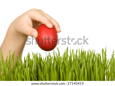 Child hand with red easter egg over green grass - isolated