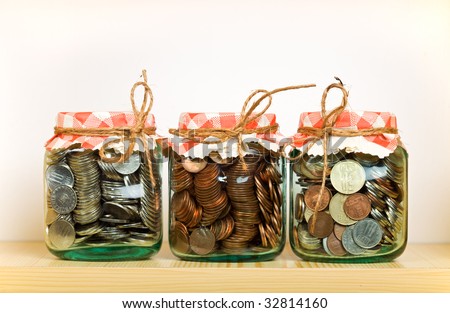 Saving money concept with coins put away in glass jars on a shelf