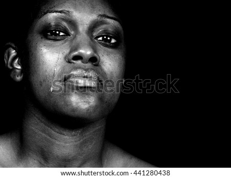Black and white portrait of a tearful African-American woman posing against a black background