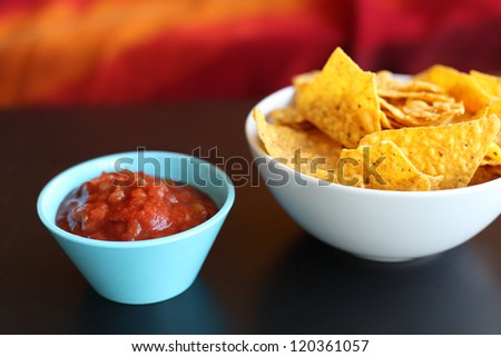 Hot red salsa and tortilla chips in bowls on black table