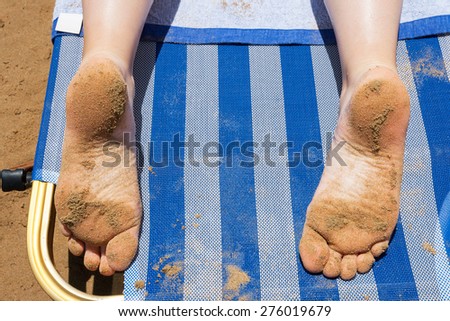 Sandy feet of girl laying on sunbed