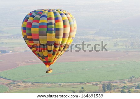 A balloon with a basket full of people flying over agricultural fields.