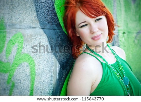 an attractive redheaded girl stands on a background graffiti on a wall