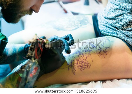 MINSK, BELARUS - SEPTEMBER 19, 2015: Professional tattoo artist doing tattoo on client leg. The 2th International Tattoo Convention