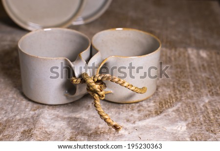 Two cups in the style of the old modernist linked site coarse rope. Cups are on the plane, covered with burlap. Knot symbolizes forever, all that husband and wife will do, they will do together