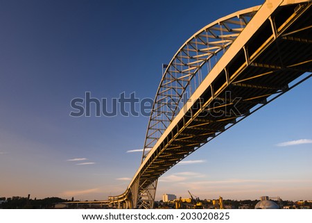 The longest in Europe and America arched Fremont Bridge Portland Oregon Willamette River. Painted metal truss road bridge view from below against the blue sky and the coastal industrial area.