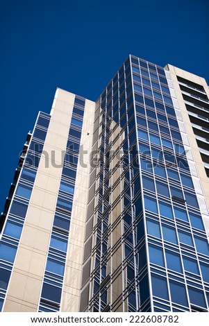 Detail of a modern high-rise multilevel building with right angles, with dark blue glass windows with metal frames and walls overlaid with natural beige travertine, with the prospect of a blue sky