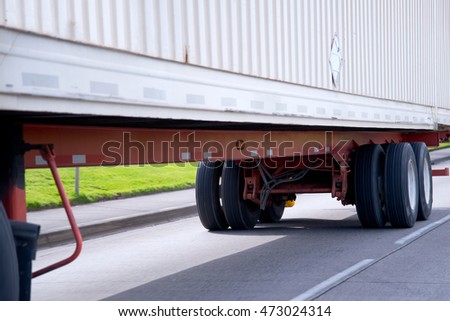 Wheels and chassis on orange frame of long commercial semi truck trailer mounted with a ribbed container for transport of dry industrial goods over long distances freights.