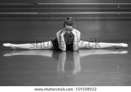 Black & White photo of a ballerina stretching her middle splits, in the studio with barre background