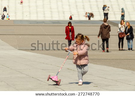 Paris, France - May 4, 2014: Paris, La Defense business district. Little girl with scooter in front of a large staircase.