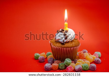 Birthday cupcake with candle on top and candies with red background