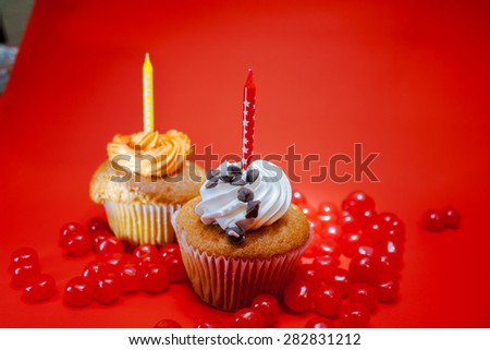 Birthday cupcake with candle on top and candies with red background