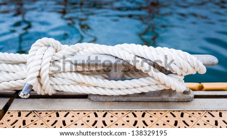 Close-up of a mooring rope with a knotted end tied around a cleat on a pier/ Nautical mooring rope
