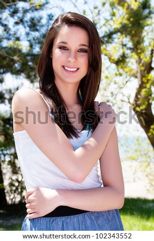 Cute brunette in casual summer clothing outdoors in summer sunshine smiling at the camera