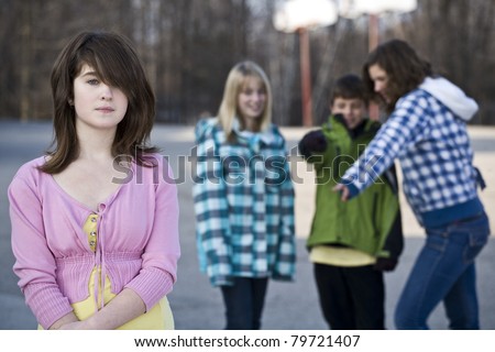 Alone in school, young girl standing away from schoolyard friends as they make fun of her behind her back
