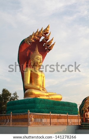 A new golden big Buddha meditation sitting outdoor in the temple (wat) area. Sky in the morning is in the background. Above the head is seven big snakes.