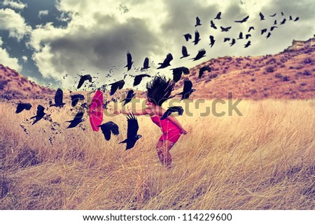 a girl in a field with an umbrella pointing toward a flock of birds