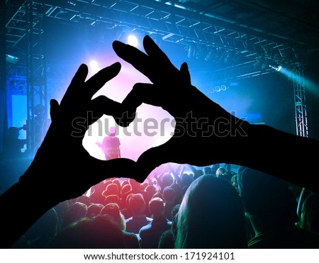 A Crowd Of People At A Concert With A Heart Shaped Hand Shadow