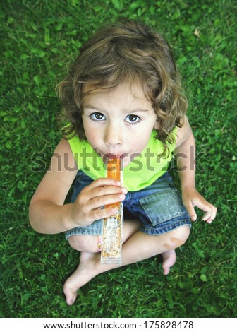 a young girl eating a frozen treat in the grass