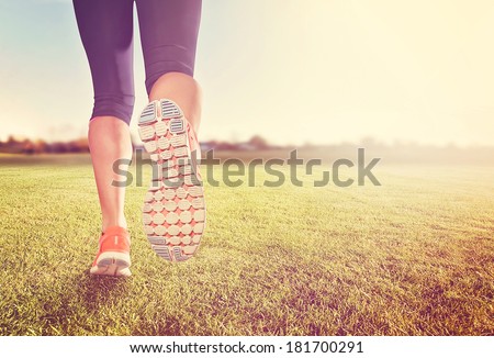 a woman with an athletic pair of legs going for a jog or run on grass during sunrise or sunset - healthy lifestyle concept done with an instagram like filter