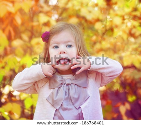 young girl sticking out her tongue in front of autumn orange leaves