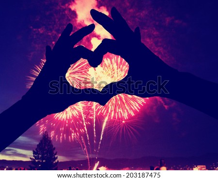 a silhouette of hands shaped in a heart against a 4th of july fireworks background
